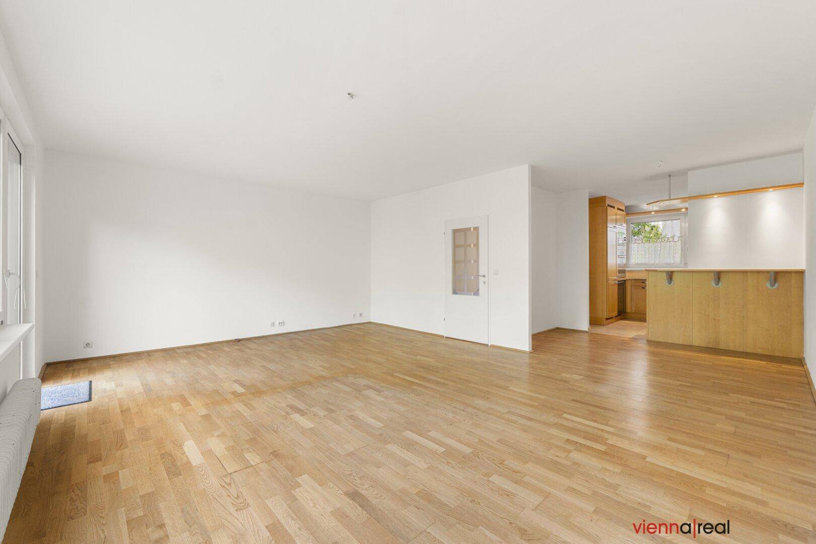 Offener Wohnbereich mit Parkettboden und weiß gestrichenen Wänden, mit angrenzender Küche und Frühstücksbar.