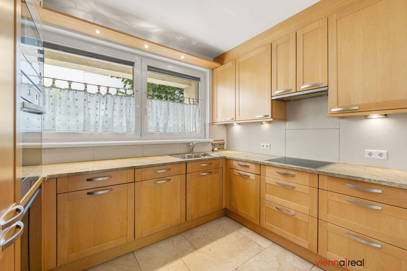 Funktionale Küche mit hellen Holzschränken, Granitarbeitsplatten und Induktionskochfeld, mit Fenster.