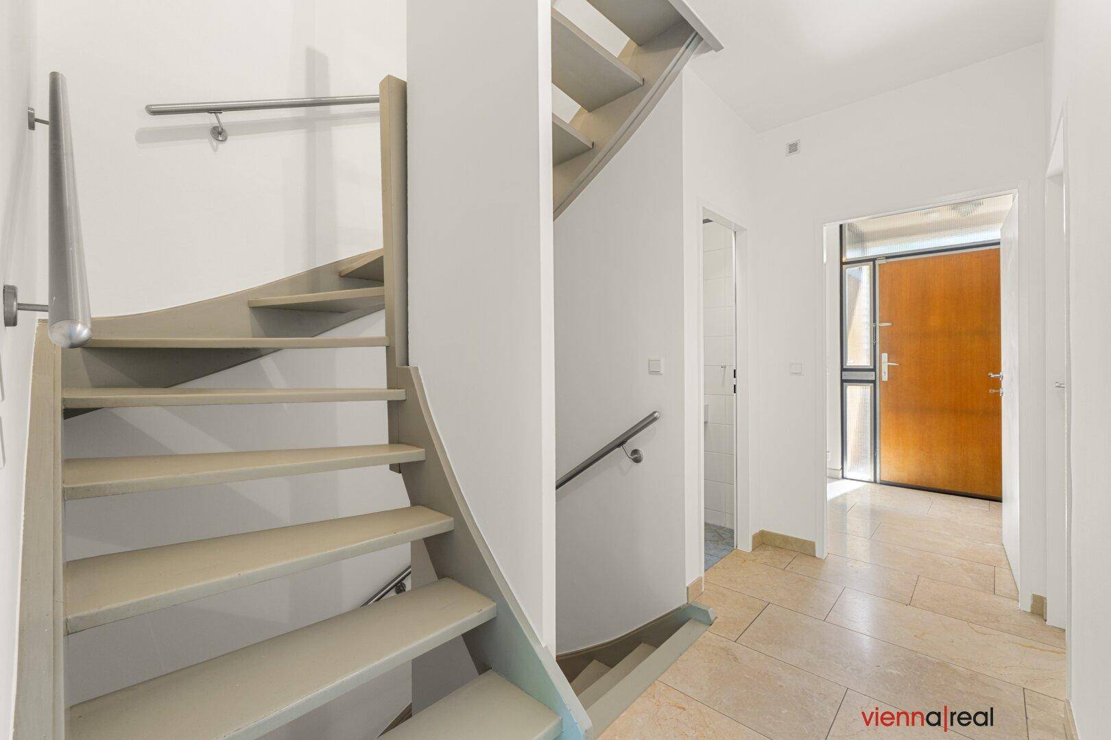 Heller Flur mit eleganter Treppe und Zugang zum Eingangsbereich, ausgestattet mit Fliesenboden.