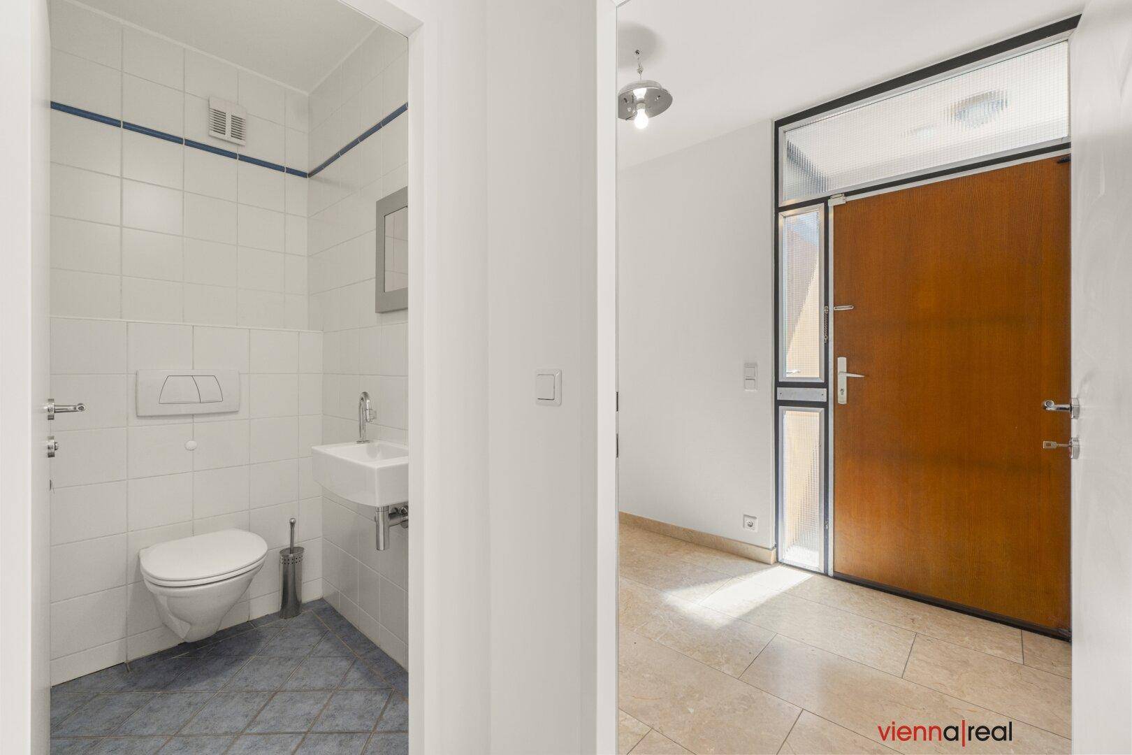 Kleines Gäste-WC mit Wand-WC und Waschbecken, angrenzend an einen hellen Eingangsbereich.