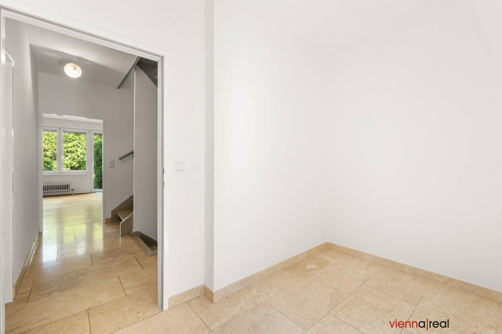 Heller Flur mit Fliesenboden und Blick auf den Wohnbereich sowie die Treppe, in schlichtem Design.