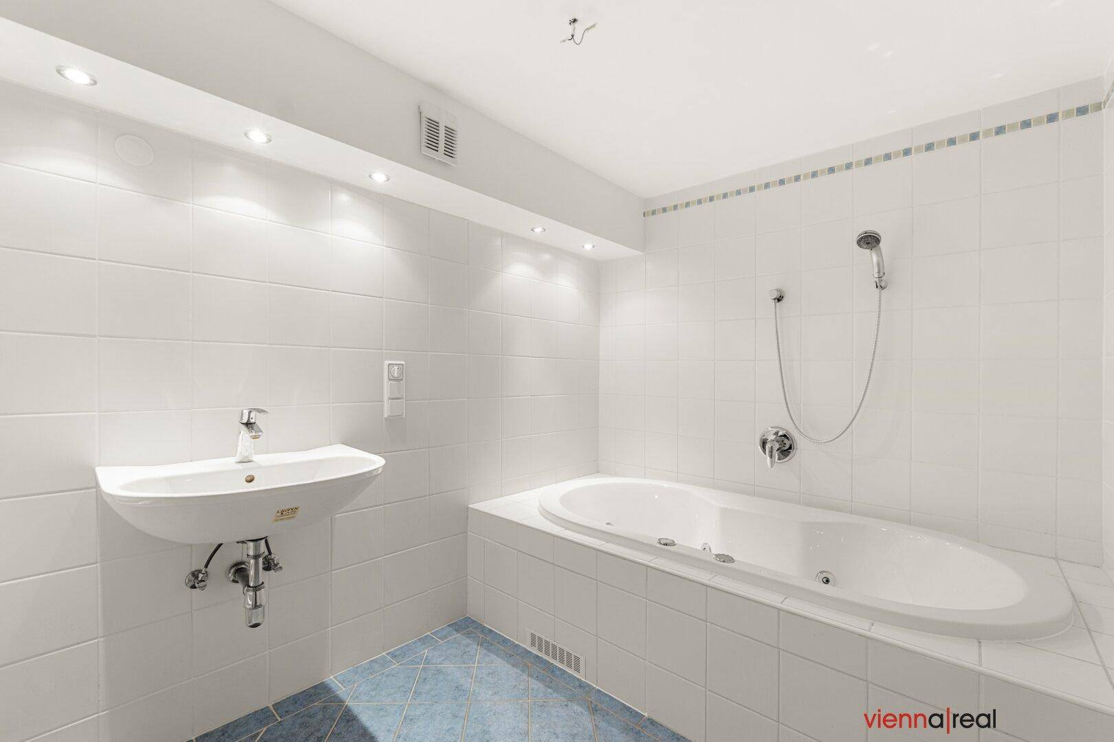 Helles Badezimmer mit eingebauter Badewanne und Waschbecken, in weißen Fliesen gehalten.