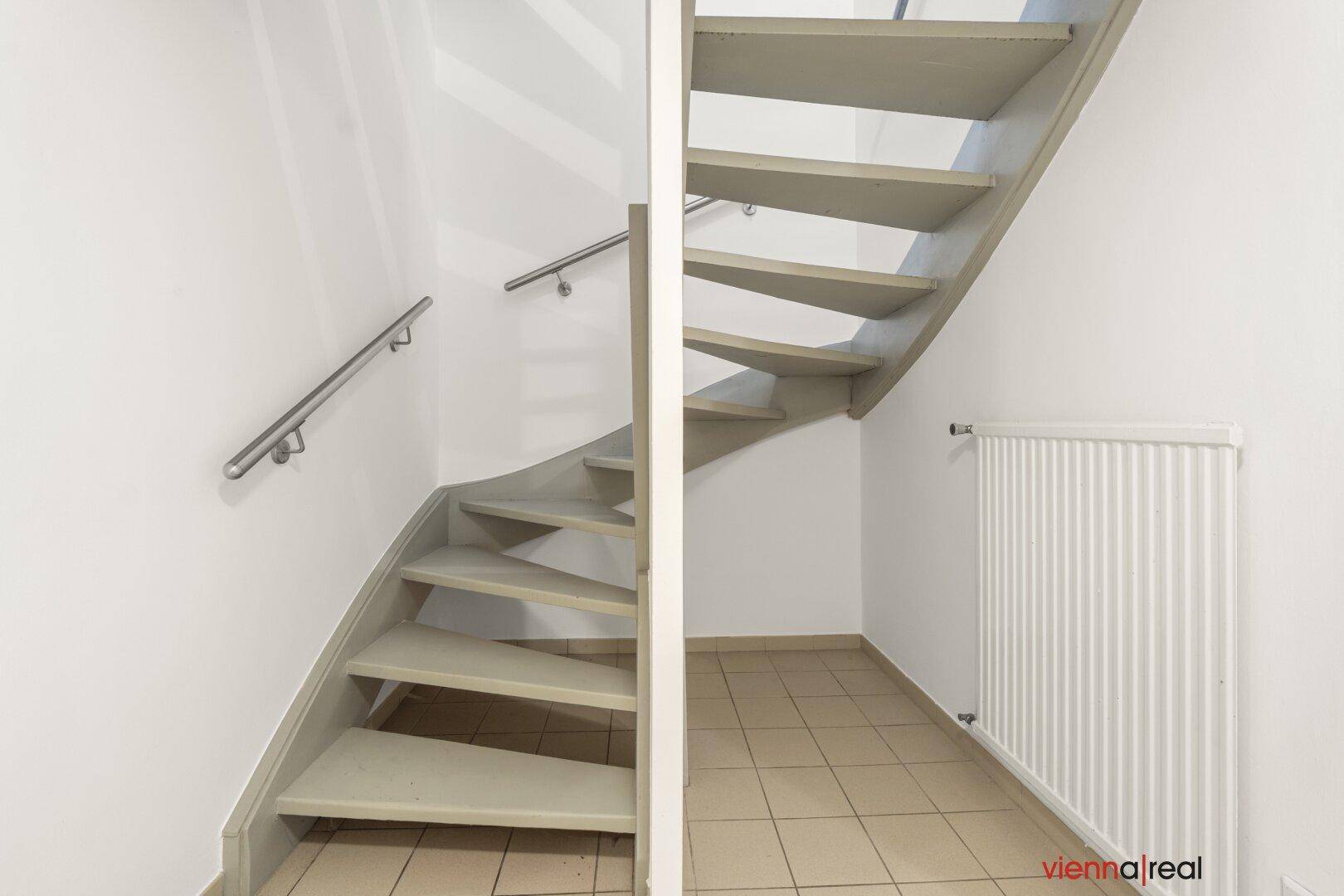 Moderne Treppe mit hellgrauen Stufen und Geländer, angrenzend an eine weiße Wand und Heizkörper.