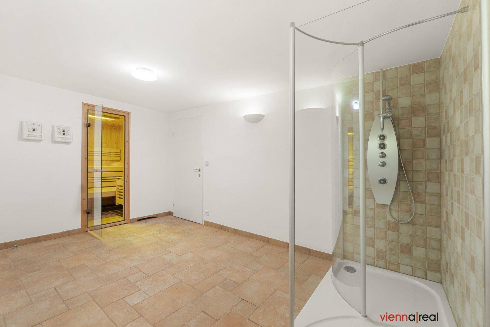 Wellnessbereich mit Duschkabine und Zugang zu einer Sauna, ausgestattet mit Fliesenboden.