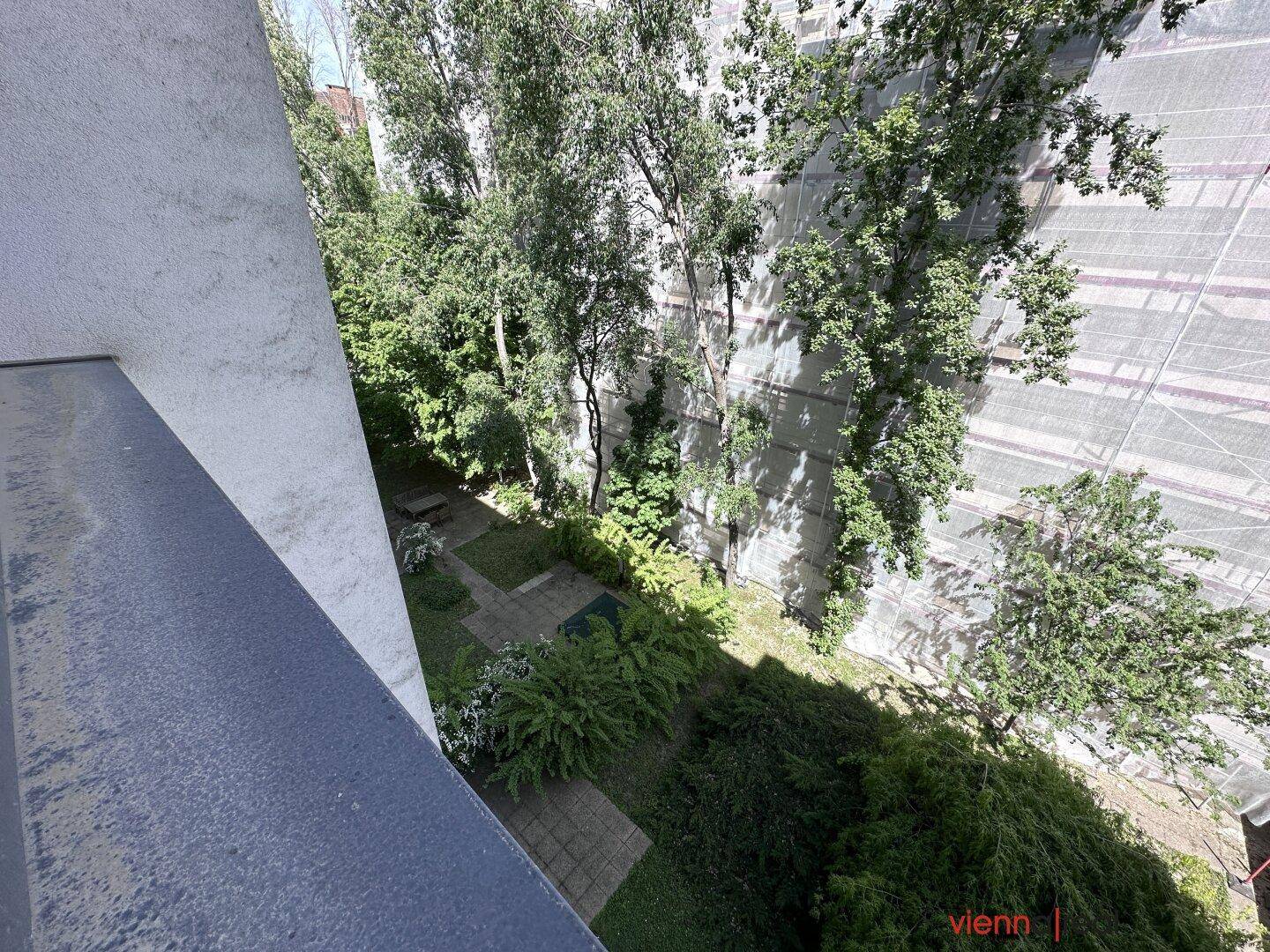 Blick auf einen begrünten Innenhof mit Gartenbereichen und Gebäuden mit Baugerüsten.