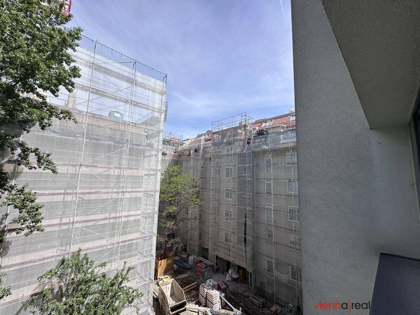 Blick auf einen Innenhof mit Baugerüsten an Gebäuden und grünen Bäumen.
