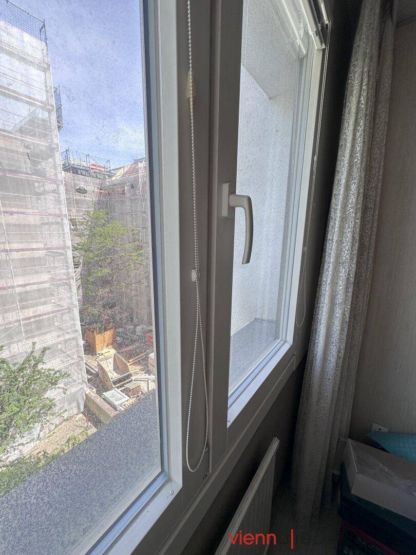 Nahaufnahme eines Fensters mit Blick auf Baugerüste und Bäume im Innenhof.