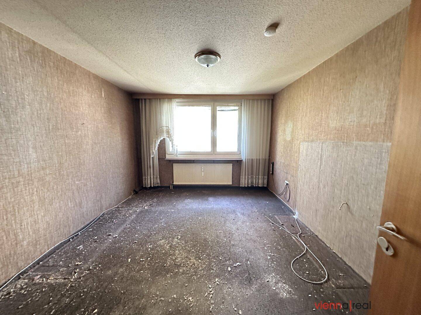 Leeres Schlafzimmer mit beschädigtem Boden und entfernter Tapete, bereit zur Renovierung.