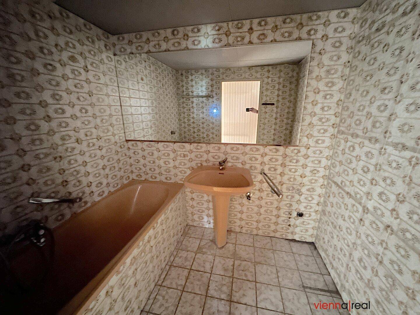 Veraltetes Badezimmer mit gemusterten Fliesen, einer Badewanne und einem Waschbecken im Originalzustand.