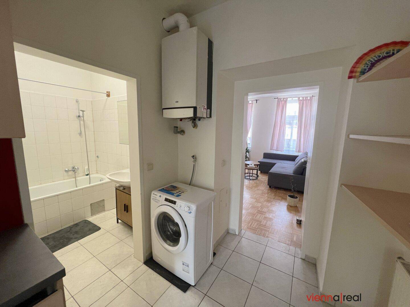 Flur mit Waschmaschine und Blick in das Badezimmer sowie den Wohnbereich.