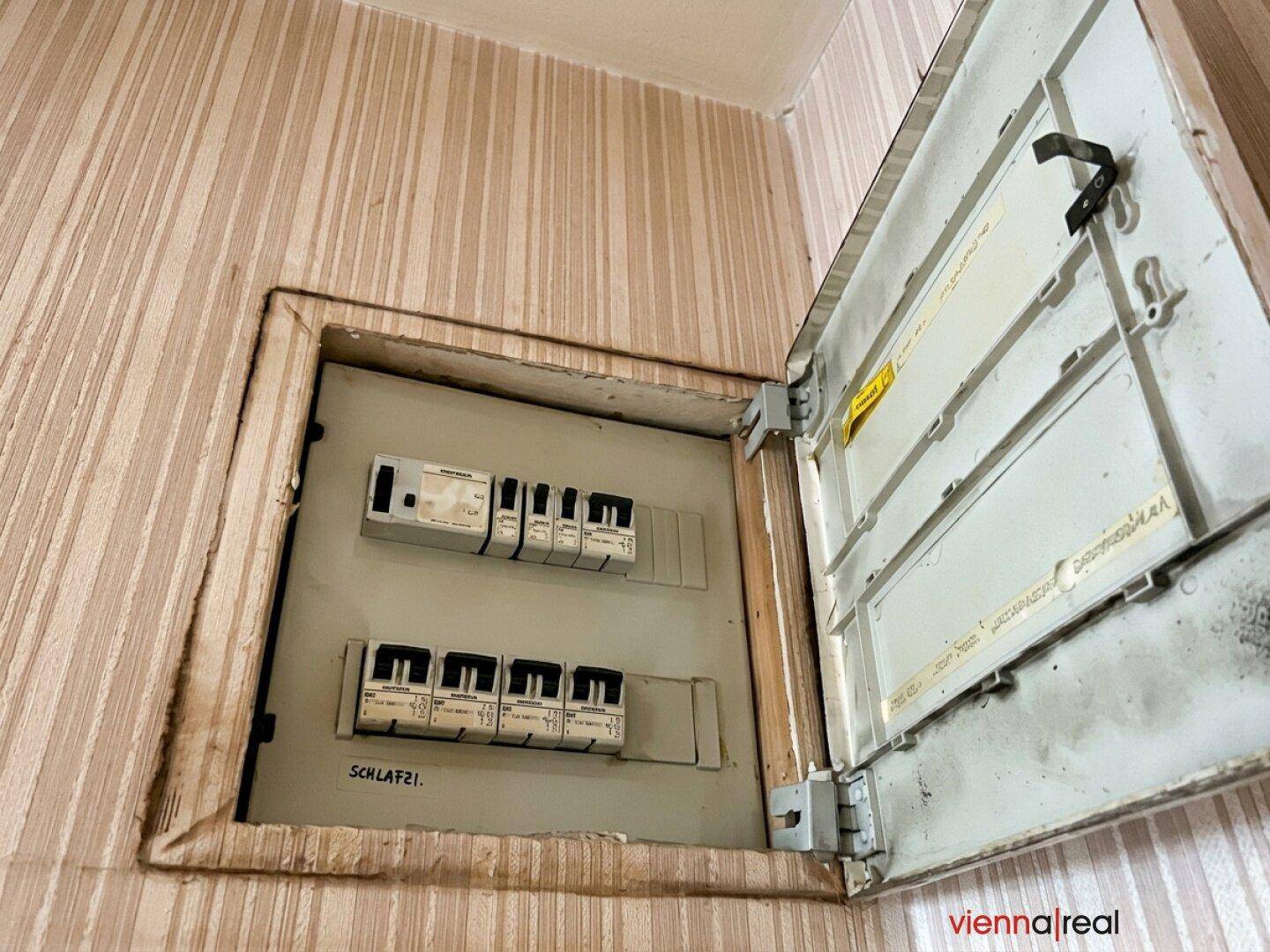 Alter Sicherungskasten mit sichtbaren Schaltern und Beschriftungen an der Wand.