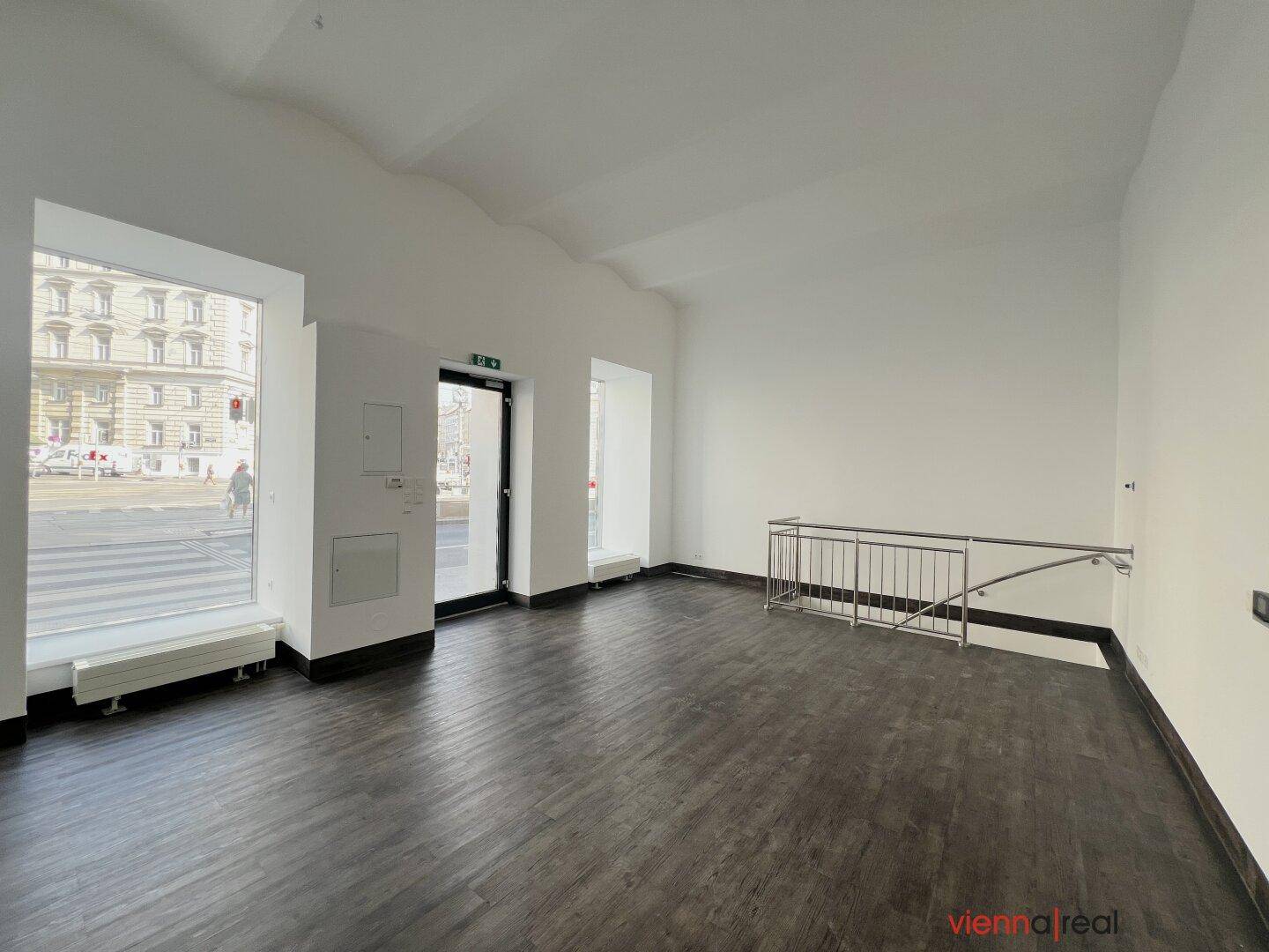 Großer Gewerberaum mit Eingangstür, Treppengeländer und viel Tageslicht durch die Fenster.