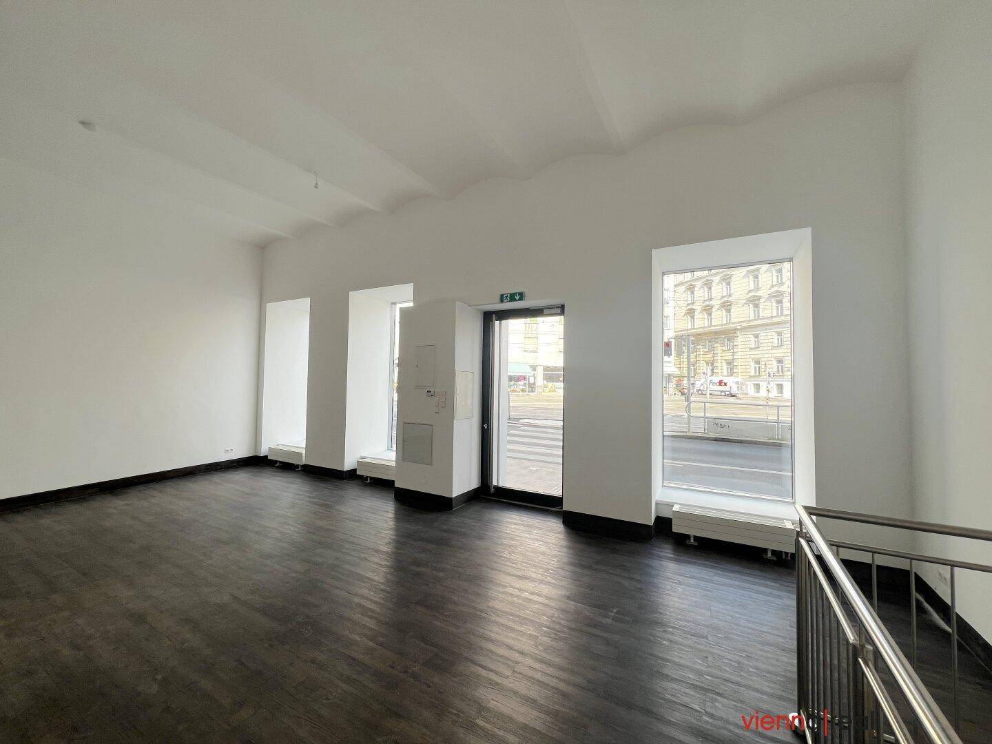 Geräumiger, leerer Gewerberaum mit dunklem Holzboden und großen Fenstern zur Straße.