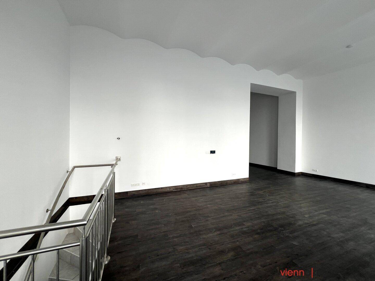 Gewerberaum mit Treppenabgang und dunklem Holzboden, ideal für verschiedene Nutzungen.