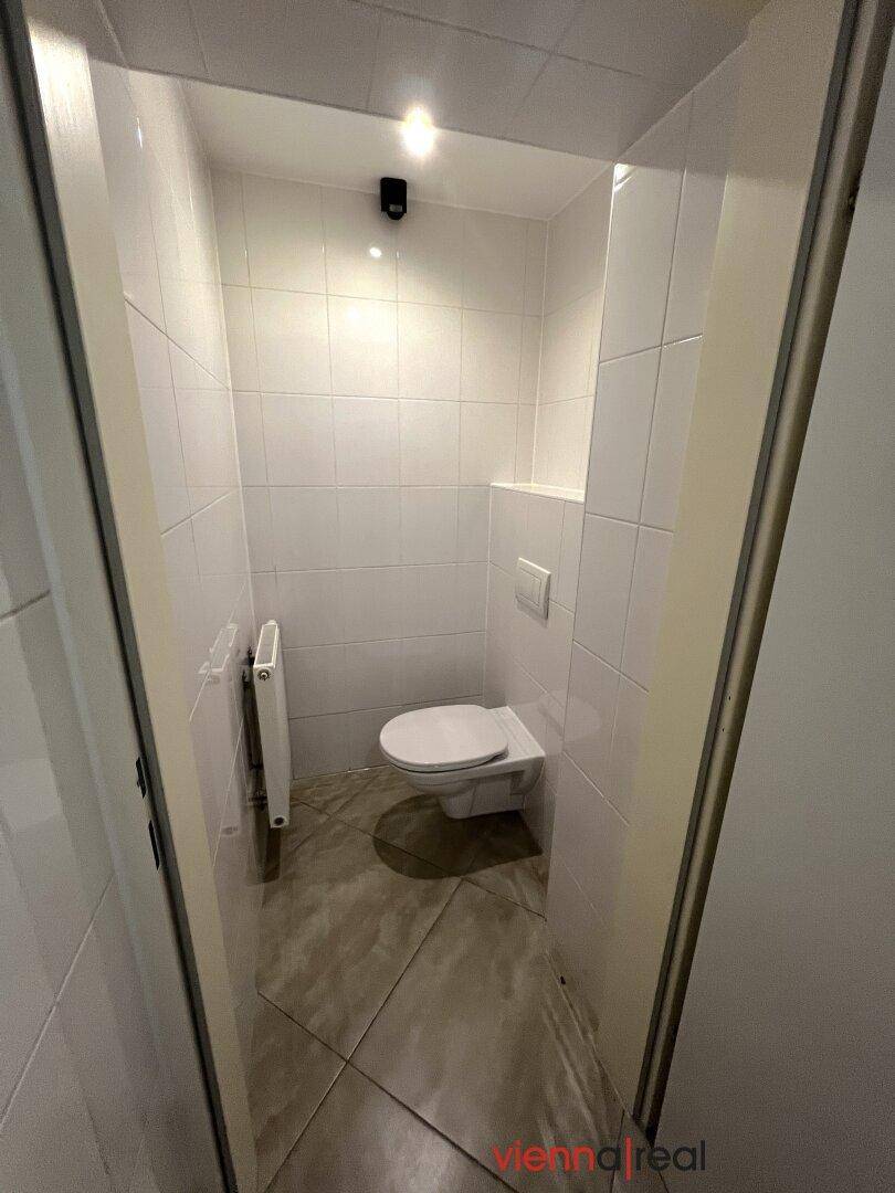 Separate Toilette mit weißen Fliesen und wandhängendem WC, modern und platzsparend.