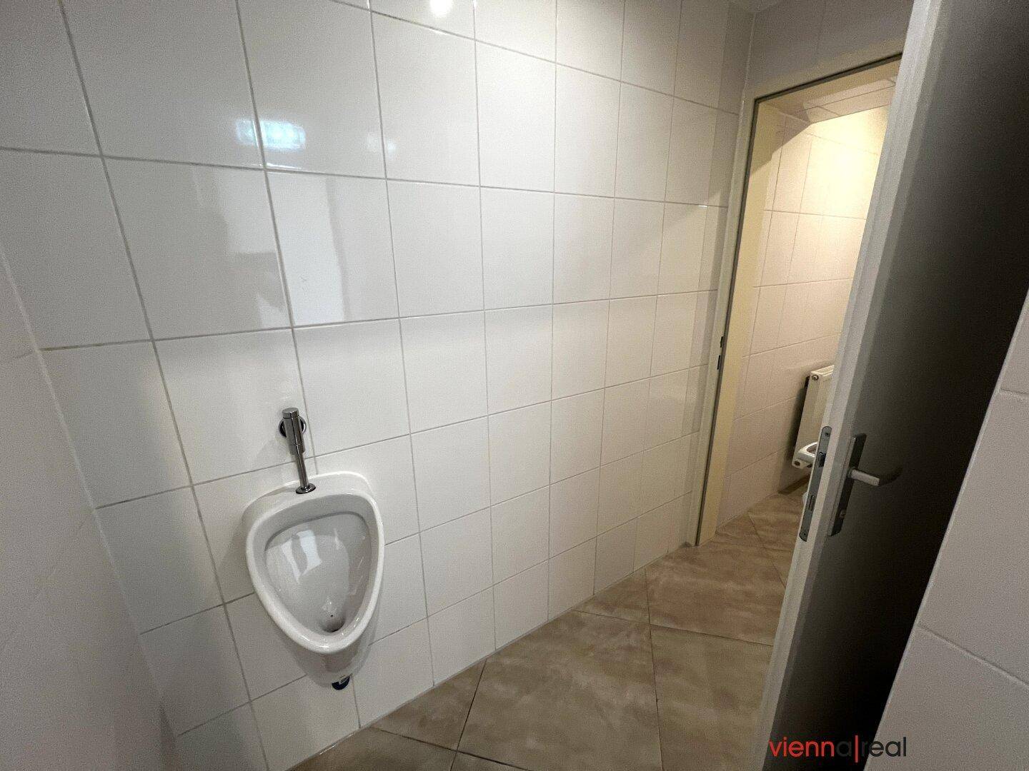 Detailansicht eines Urinals in einem hell gefliesten Badezimmer, sauber und funktional.