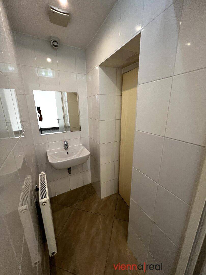 Badezimmer mit Waschbecken, Spiegel und weißen Fliesen, bietet grundlegende Ausstattung.