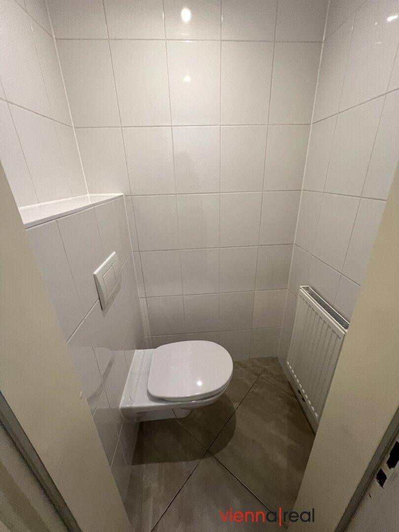 Saubere Toilette mit weißen Fliesen und wandhängendem WC, gut gepflegt und hell.