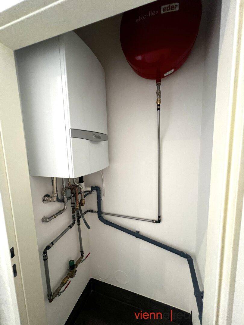 Technikraum mit Warmwasserbereiter und sichtbaren Rohrleitungen, ordentlich installiert.