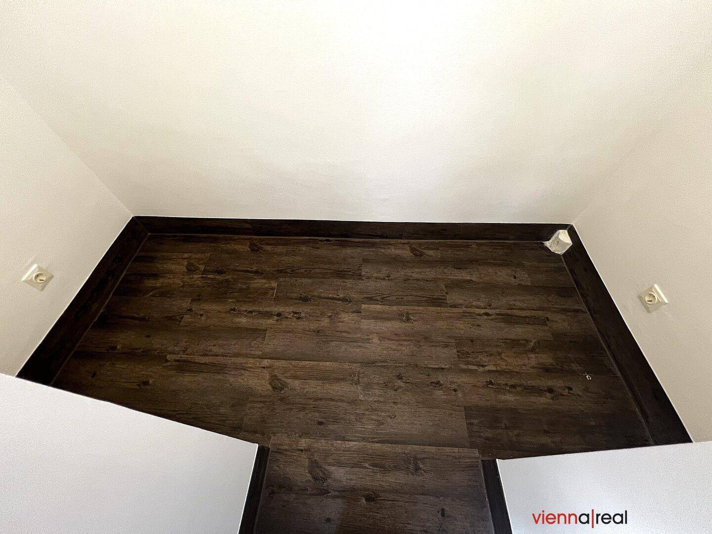 Blick von oben in einen kleinen, leeren Raum mit dunklem Holzboden und weißen Wänden, vielseitig nutzbar.