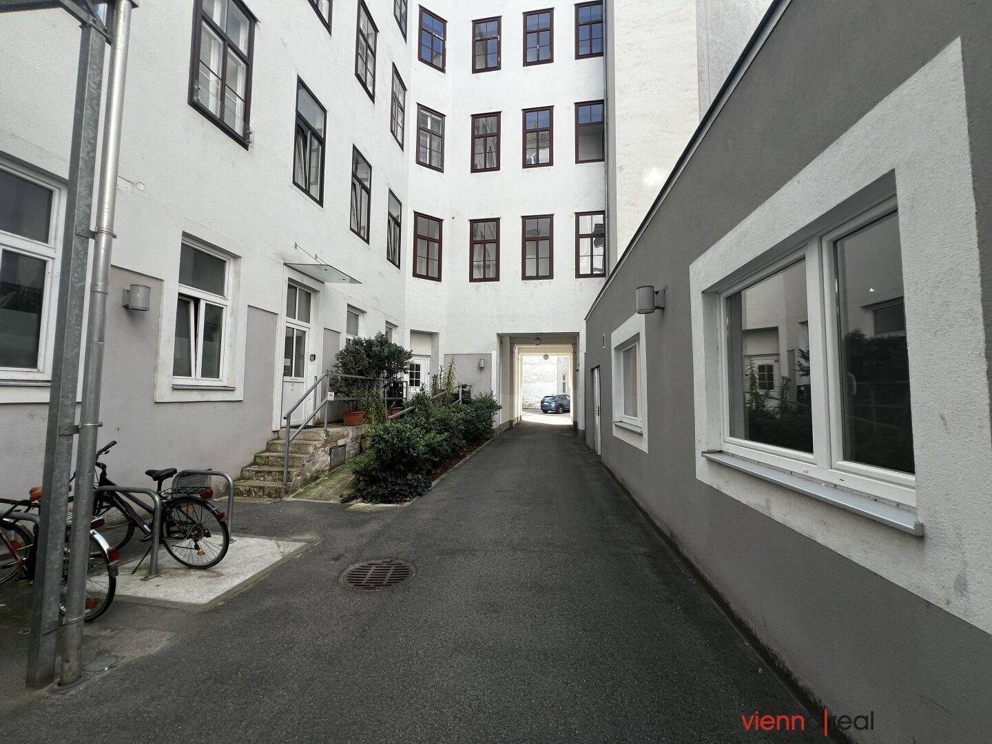Innenhof mit gepflastertem Weg, Grünflächen und abgestellten Fahrrädern, umgeben von historischen Gebäuden.