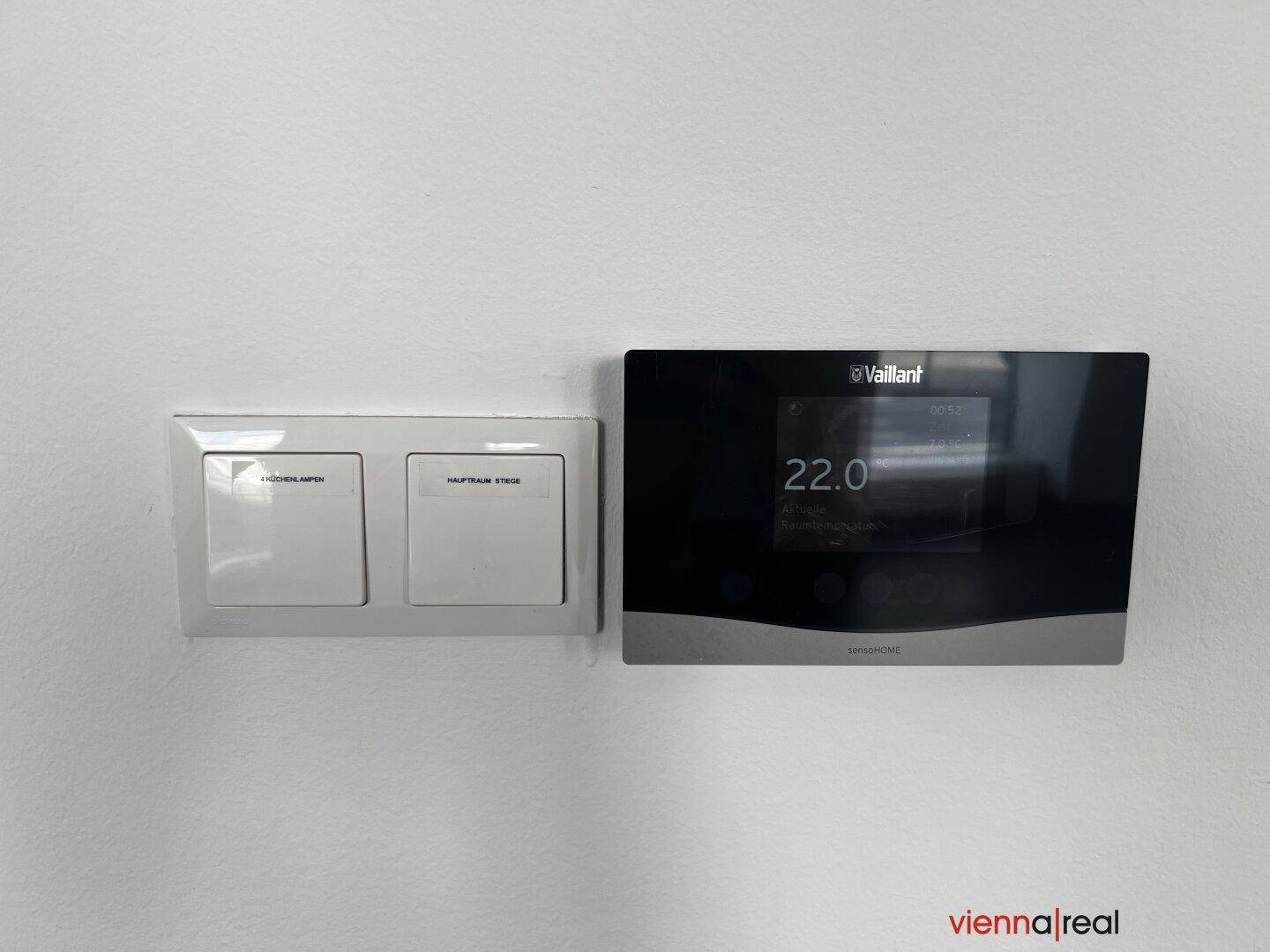 Moderner Vaillant Thermostat und Lichtschalter an einer weißen Wand, zur Klimasteuerung.