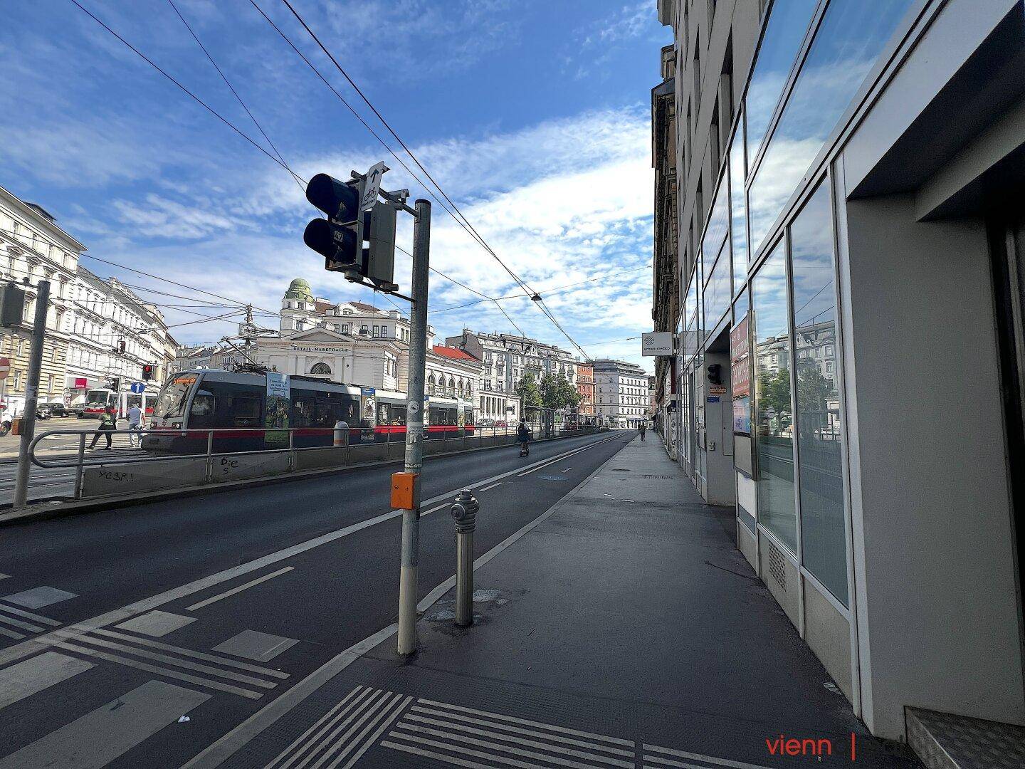 Straßenansicht mit Straßenbahn, Ampel und Gebäuden entlang der Fahrbahn unter klarem Himmel.