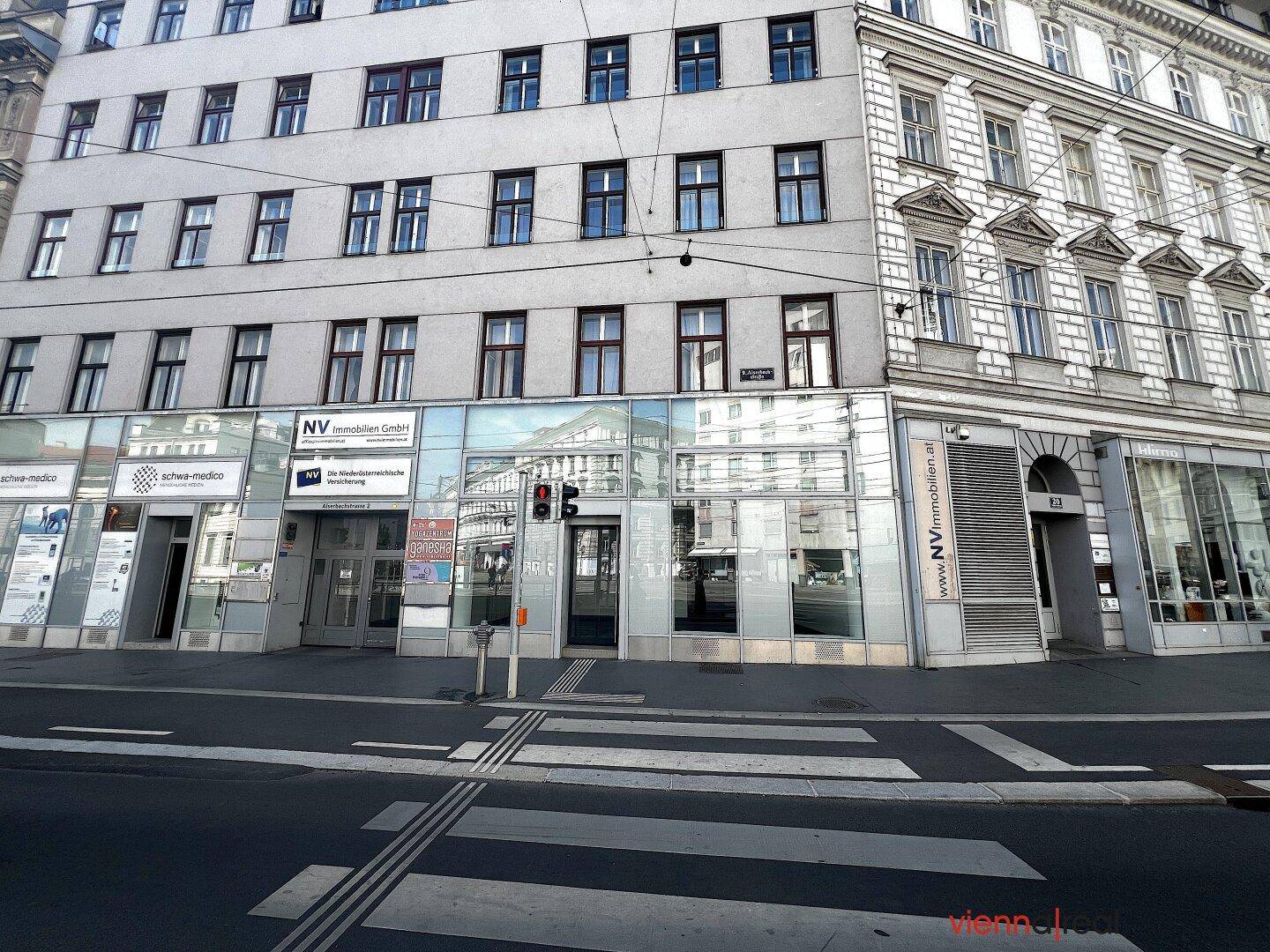 Straßenansicht einer Geschäftsfassade mit großen Schaufenstern und modernen Ladenlokalen im Erdgeschoss.