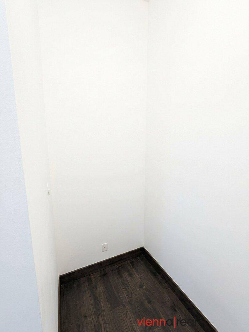 Kleiner, leerer Abstellraum mit weißen Wänden und dunklem Holzboden, ideal für zusätzlichen Stauraum.