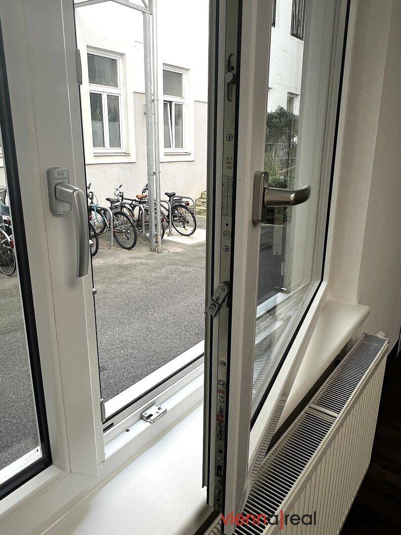 Geöffnetes Fenster mit Blick auf den Innenhof und abgestellte Fahrräder, darunter ein Heizkörper.