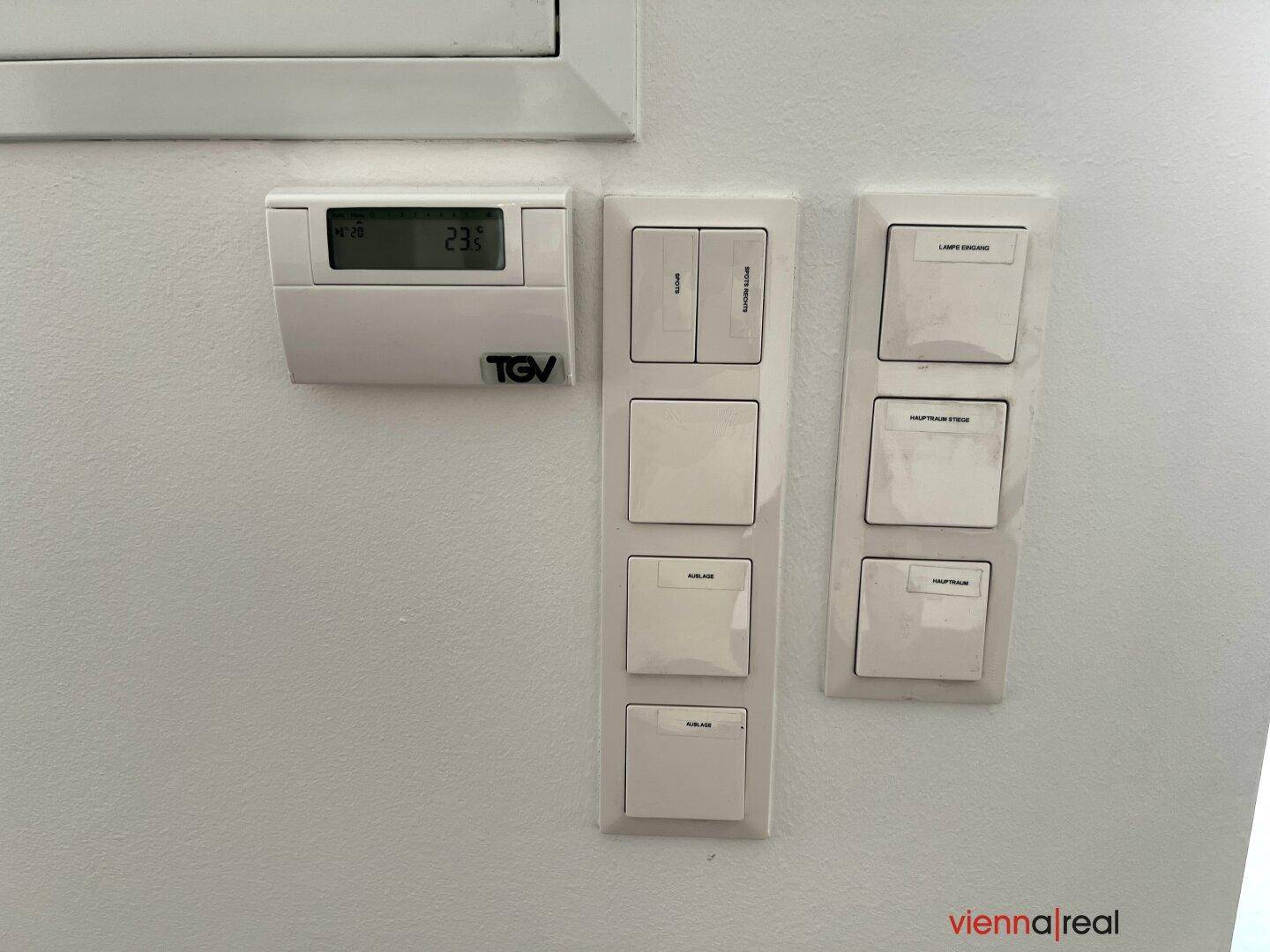 Detailaufnahme von Lichtschaltern und einem Thermostat an einer weißen Wand.