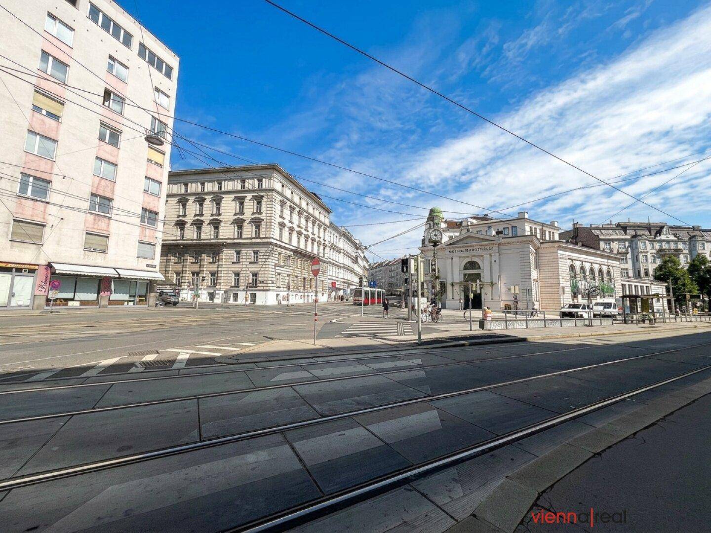 Weitläufige Kreuzung mit Straßenbahnschienen und verschiedenen Gebäuden unter blauem Himmel.