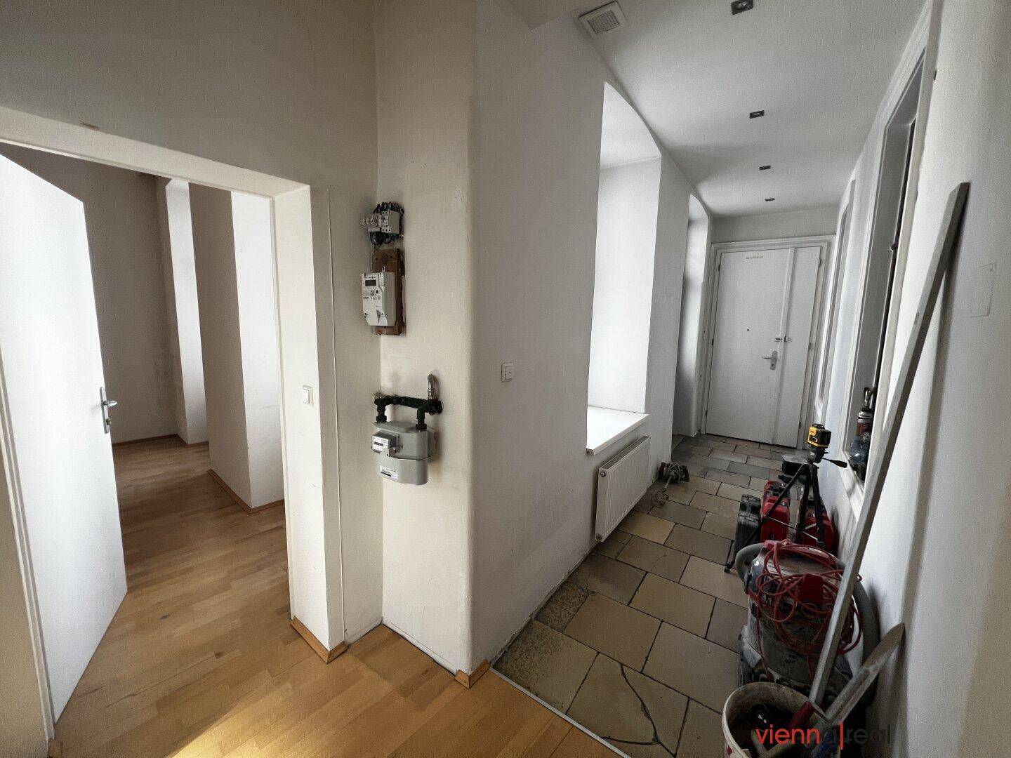 Eingangsbereich mit Fliesenboden und Blick auf die Eingangstür des Gebäudes, mit Baustellenmaterial.