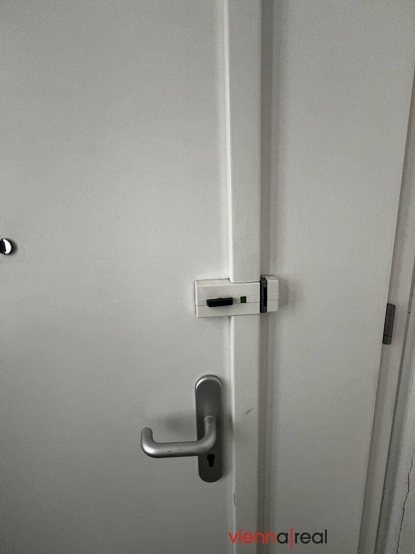 Nahaufnahme einer weißen Innentür mit modernem Türgriff und zusätzlichem Sicherheitsschloss.