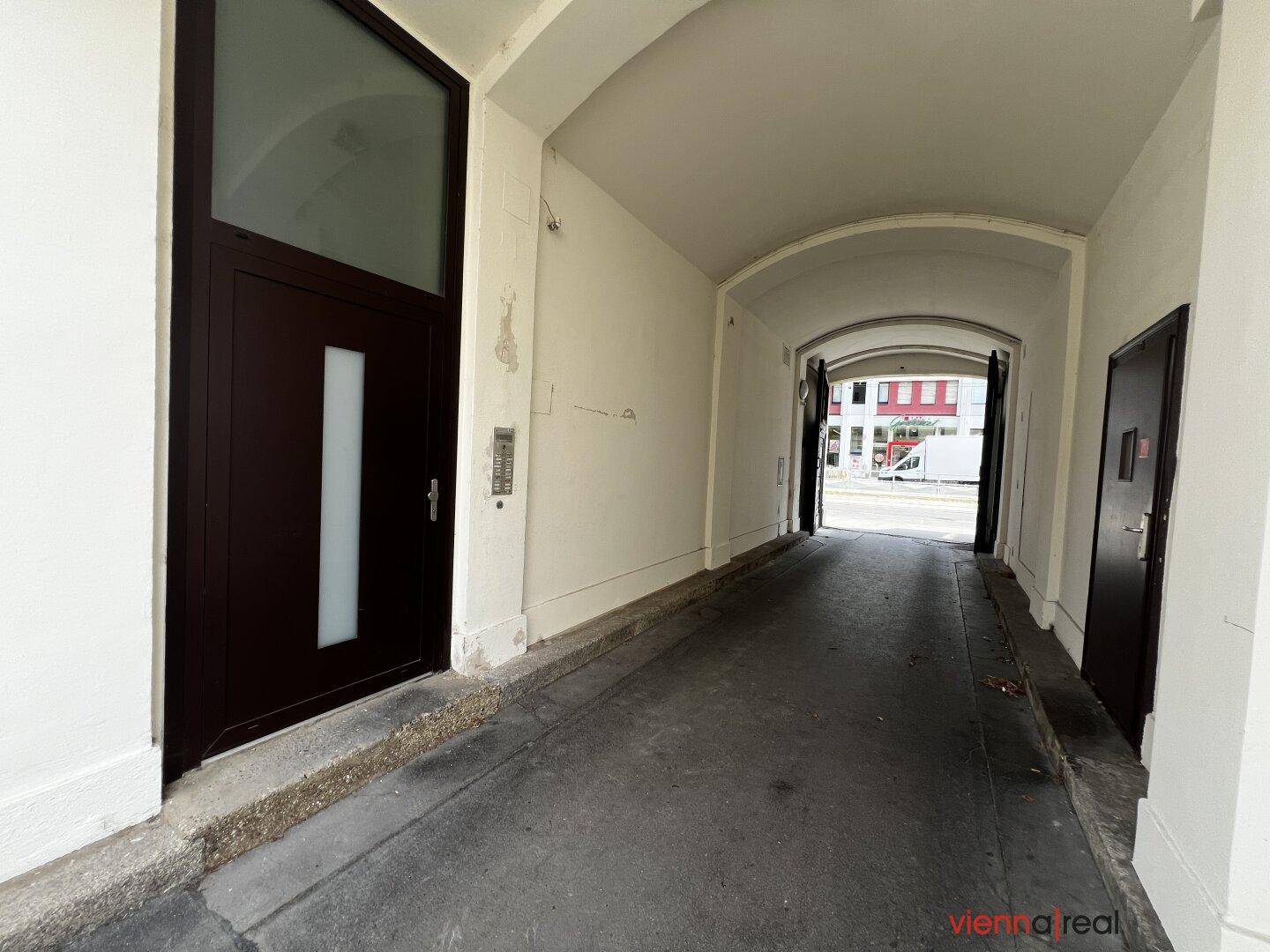 Gebäudedurchgang mit dunkler Eingangstür und Blick auf die belebte Straße.
