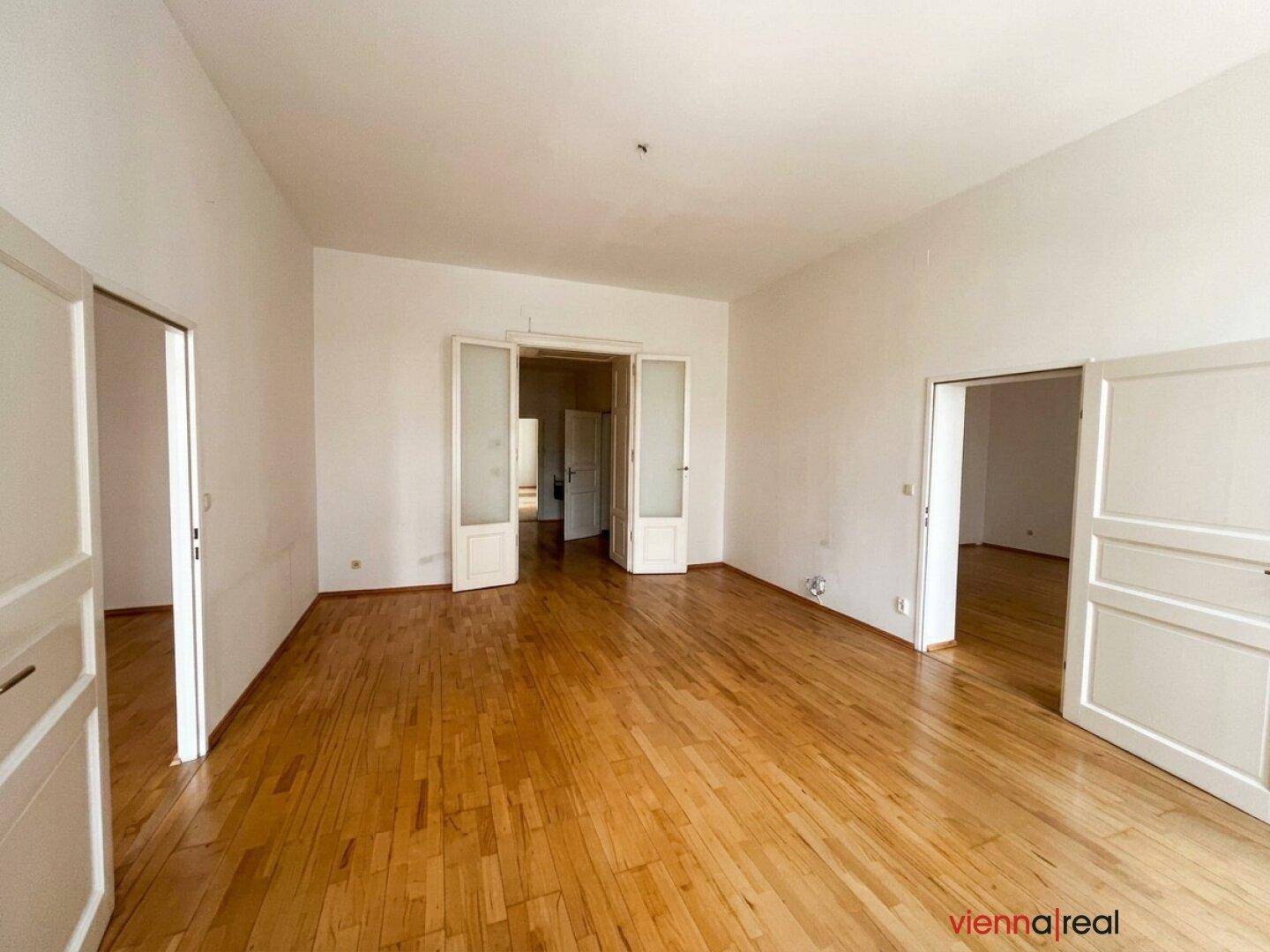 Geräumiges Zimmer mit Holzboden und mehreren Türen, das vielseitige Nutzungsmöglichkeiten bietet.