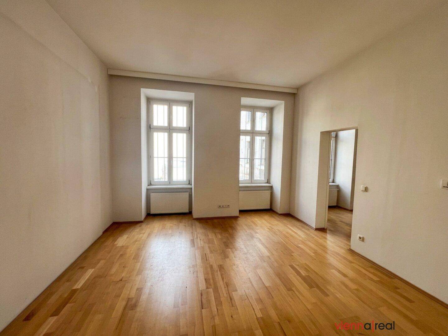 Heller, leerer Raum mit Holzboden und zwei hohen Fenstern, bereit zur individuellen Gestaltung.