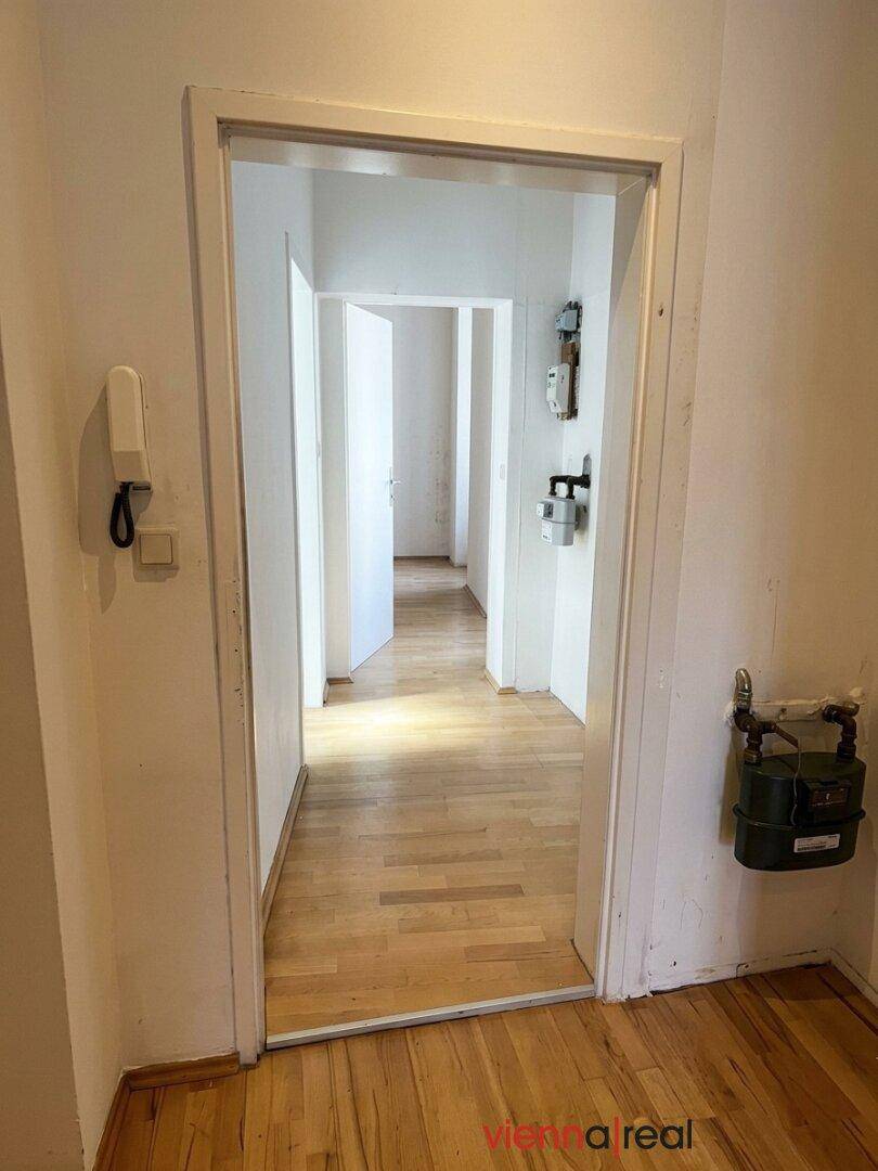 Langer, heller Flur mit Holzboden und weißen Wänden, der zu weiteren Räumen führt.