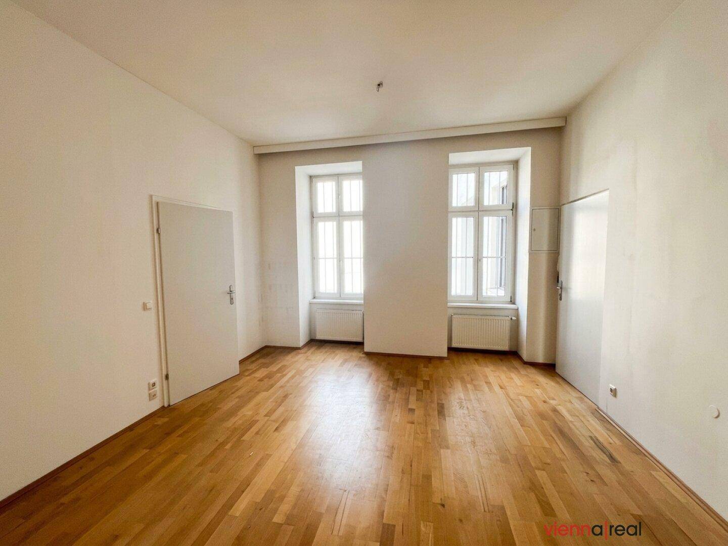 Geräumiges Zimmer mit Parkettboden und zwei Fenstern, das eine angenehme Wohnatmosphäre bietet.