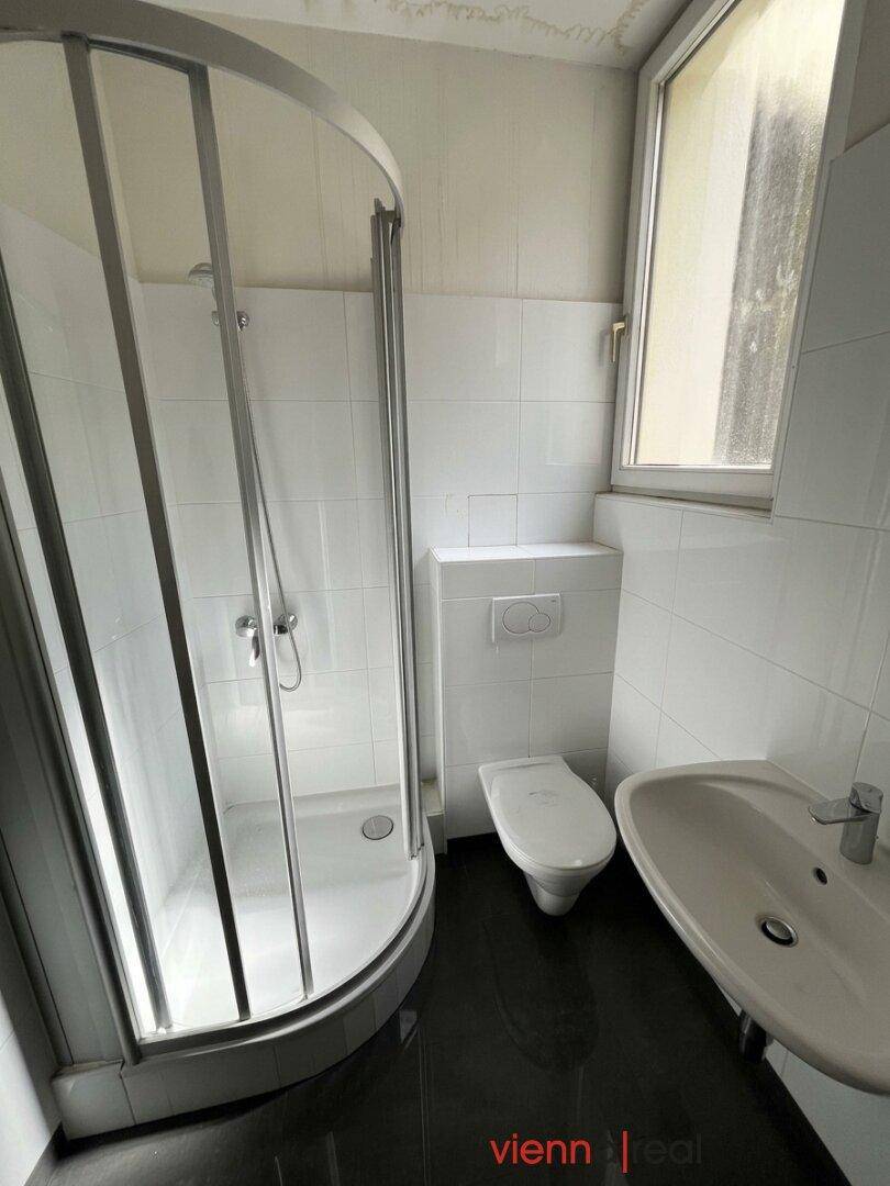 Helles Badezimmer mit Duschkabine, Toilette und Waschbecken, ausgestattet mit einem Fenster.