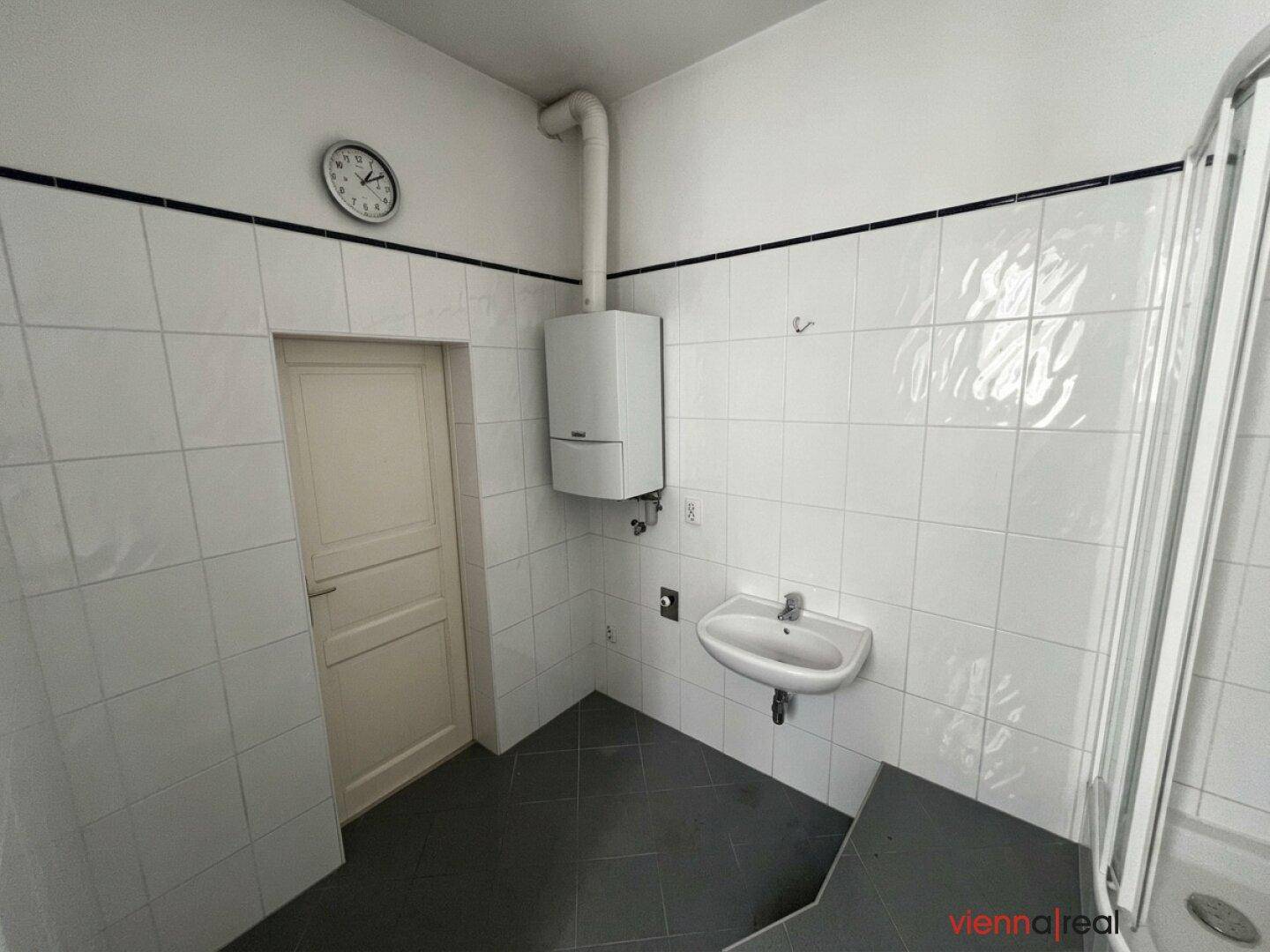 Gefliestes Badezimmer mit Duschkabine, Waschbecken und Gastherme, funktional und hell.