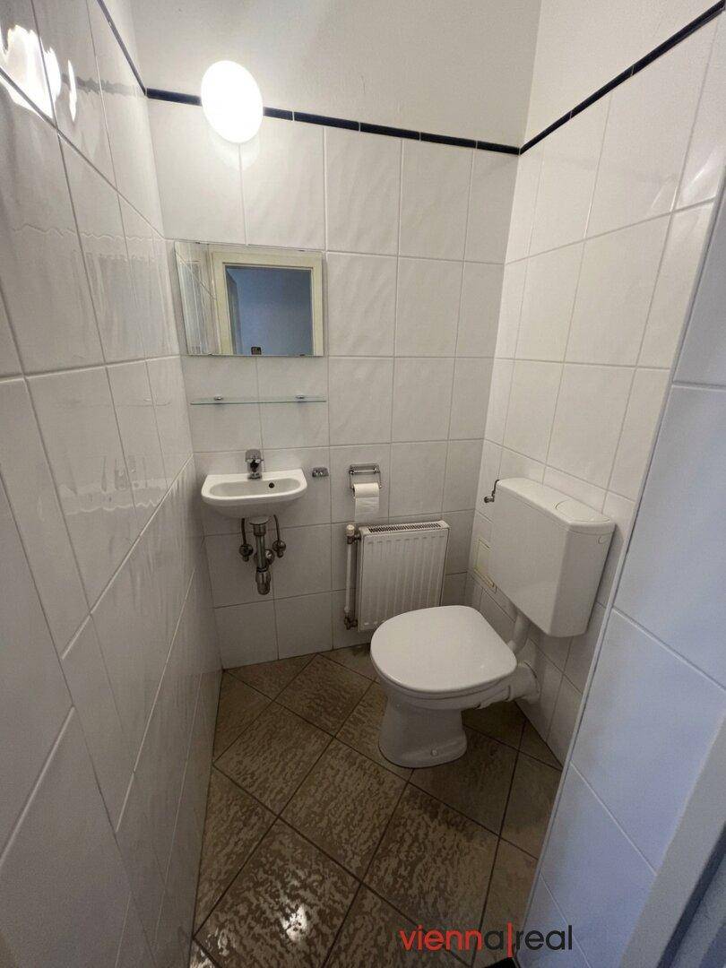 Kleines, gefliestes Gäste-WC mit Toilette, Waschbecken und Spiegel, praktisch und sauber.