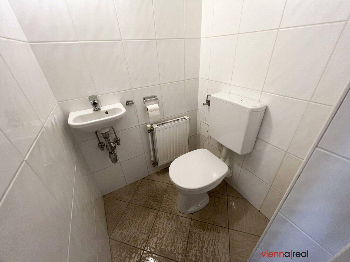 Kompaktes Gäste-WC mit Toilette, kleinem Waschbecken und Heizkörper, ideal für Besucher.