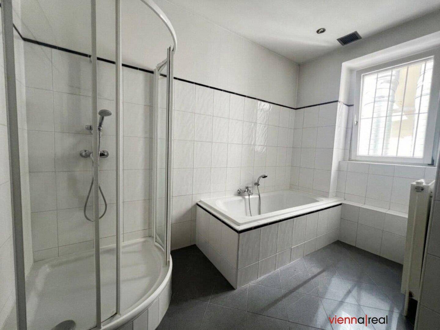 Badezimmer mit weiß gefliesten Wänden, Badewanne, Duschkabine und Fenster für Tageslicht.