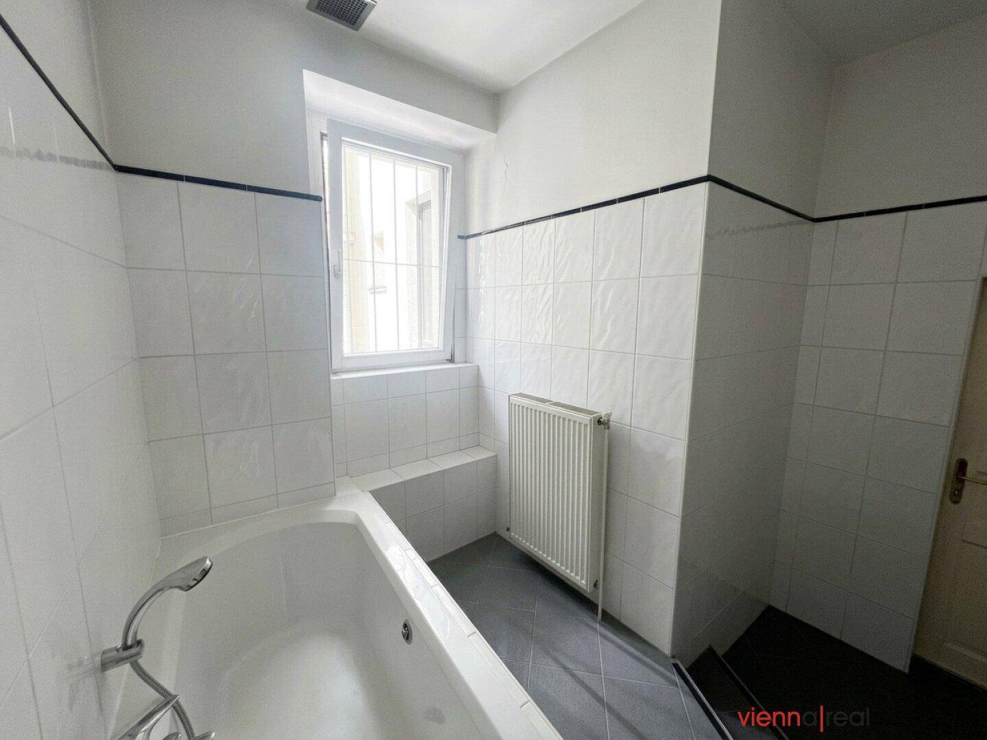 Helles Badezimmer mit Badewanne, Heizkörper und Fenster, das eine angenehme Atmosphäre schafft.