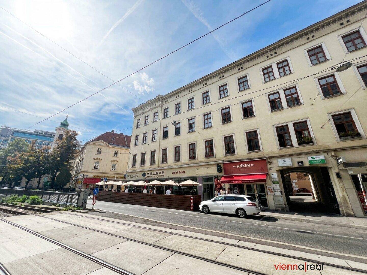 Straßenansicht eines Gebäudes mit Geschäften und einem Restaurant im Freien unter blauem Himmel.