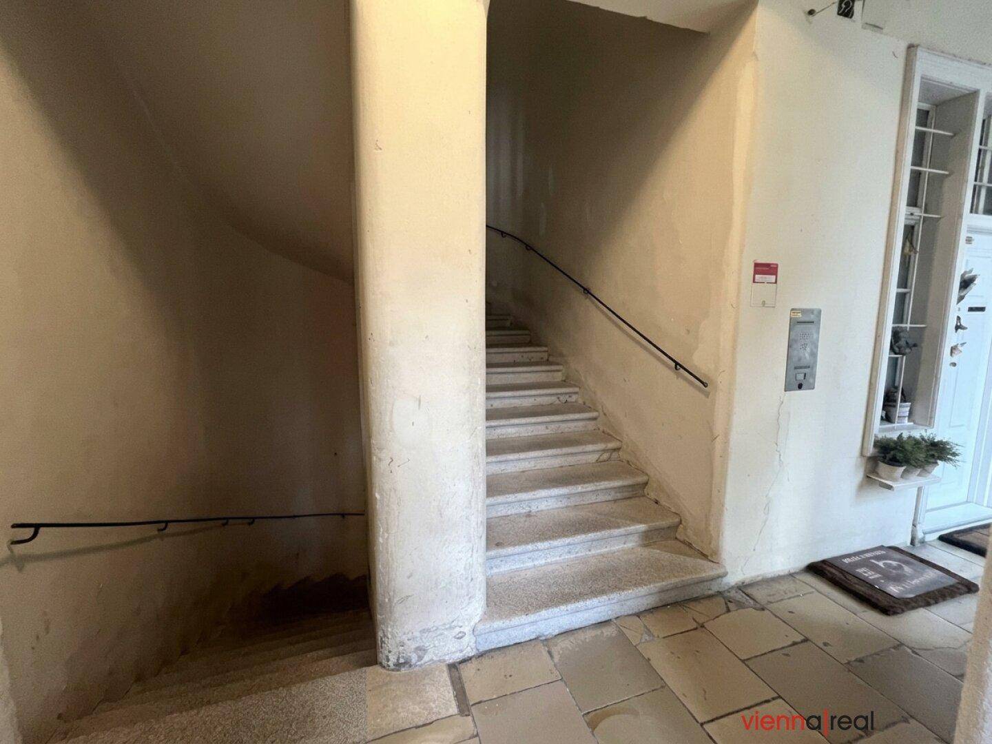Historisches Treppenhaus mit Steinstufen und schlichtem Geländer in einem Altbau.