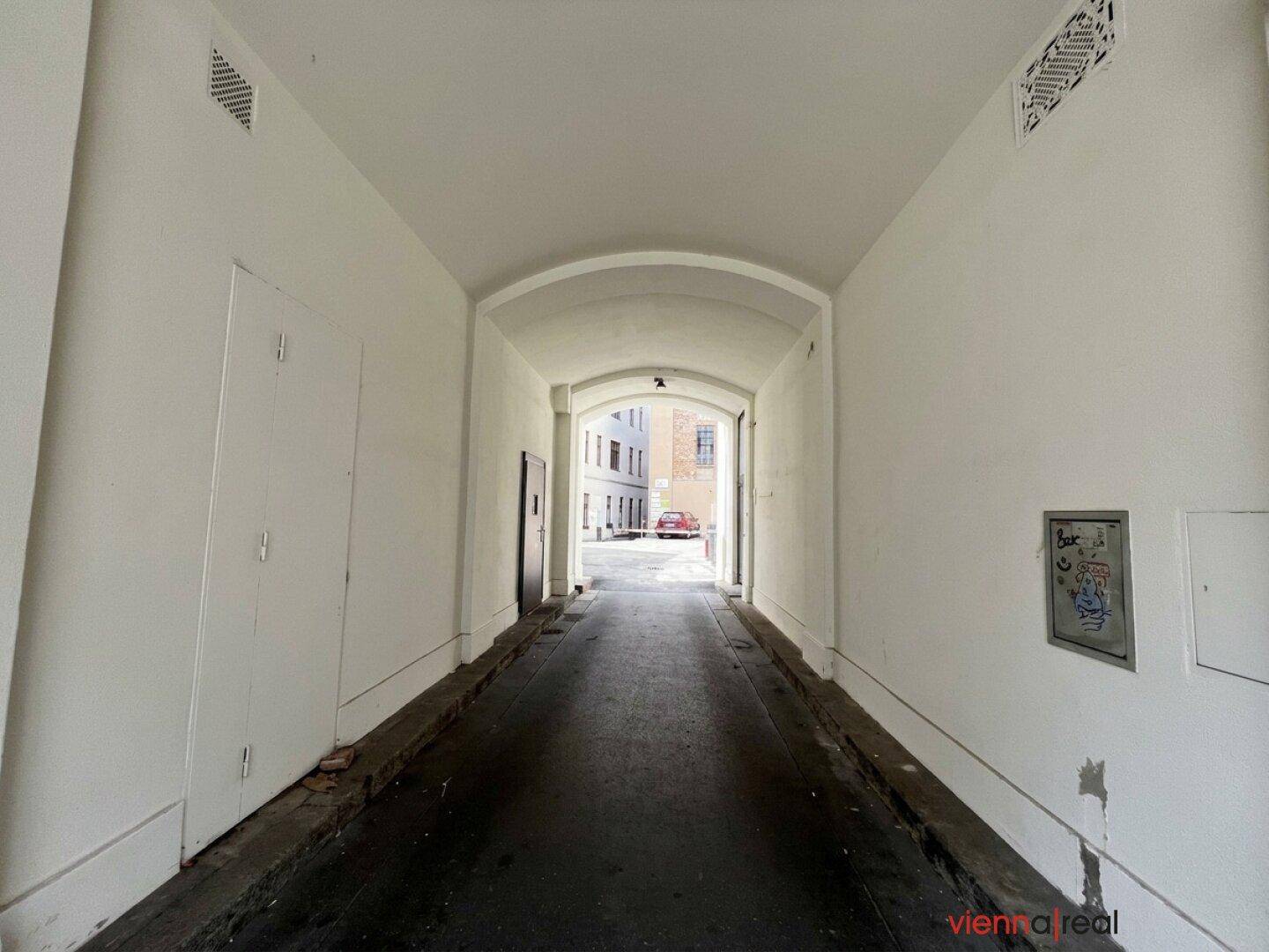 Langer, weiß gestrichener Durchgang, der zu einem Innenhof des Gebäudes führt.