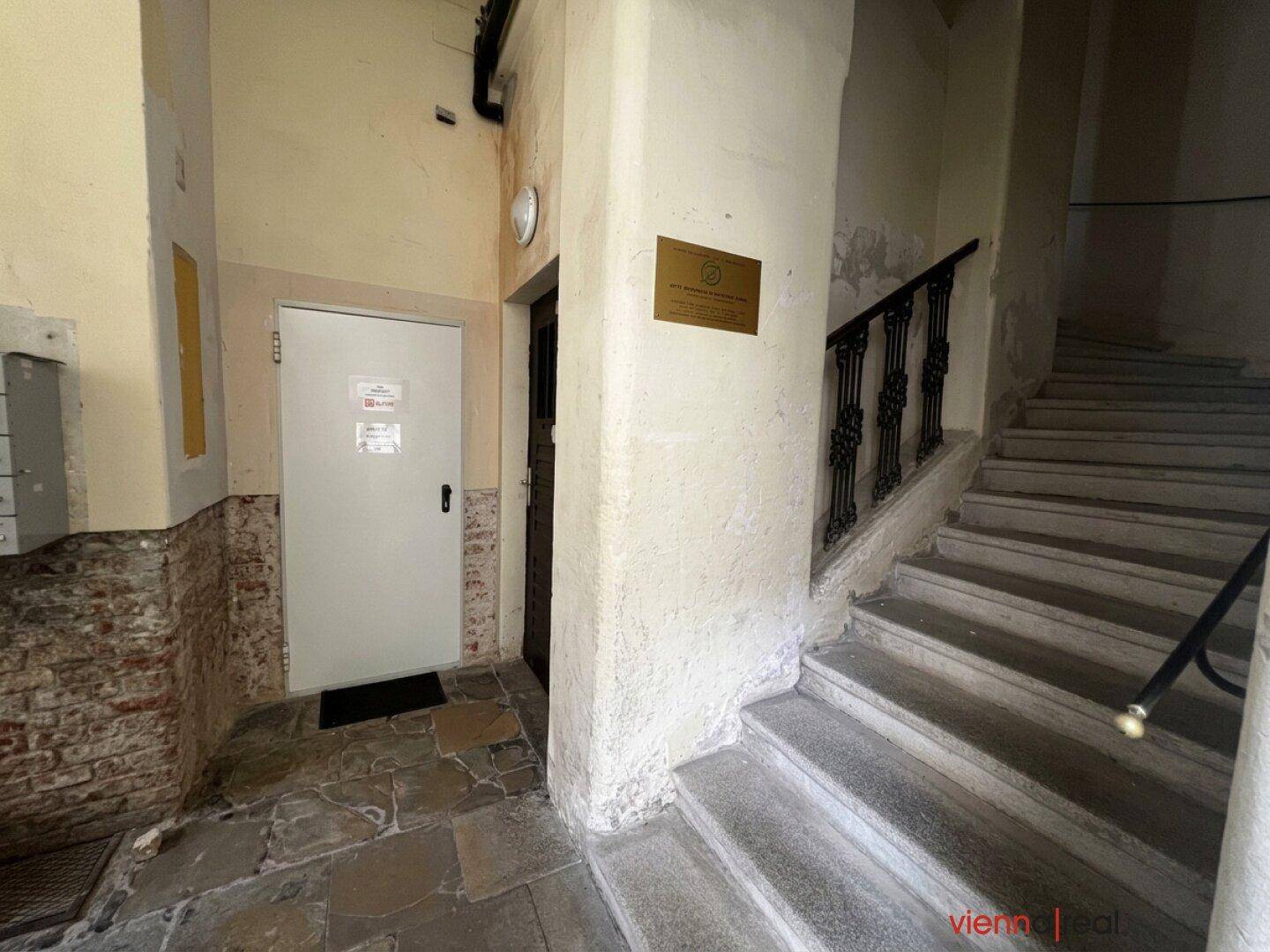 Eingangsbereich mit Treppenaufgang, Fliesenboden und einer Sicherheitstür im Altbau.