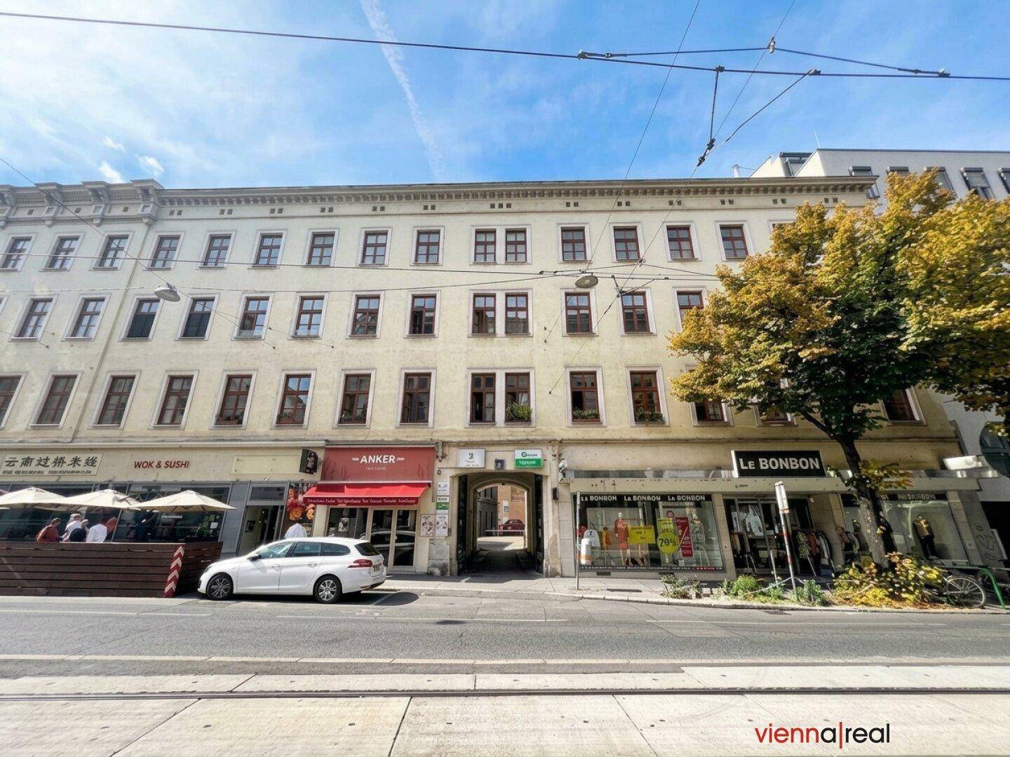 Straßenansicht eines Mehrfamilienhauses mit Geschäften im Erdgeschoss und Straßenbahnlinien.